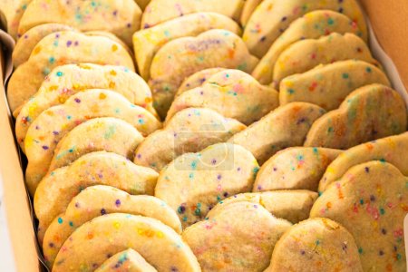 Photo for The sugar cookies, filled with sprinkles mixed into the dough, are carefully arranged with meticulous precision into a rustic brown paper box. - Royalty Free Image