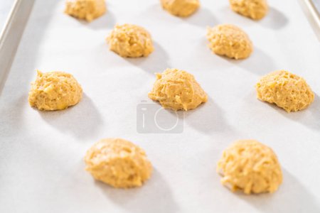 Téléchargez les photos : Ramasser la pâte à biscuits avec la pelle à pâte dans une plaque à pâtisserie doublée de papier sulfurisé pour cuire les biscuits à la banane avec de la bruine de chocolat. - en image libre de droit