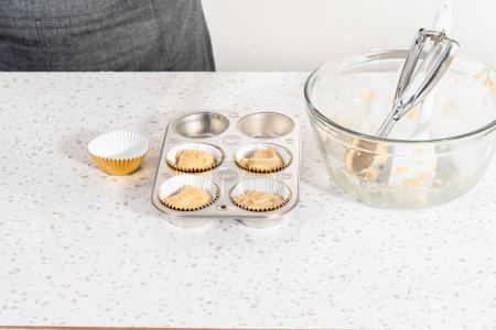 Téléchargez les photos : Scooping pâte cupcake avec cuillère à pâte dans une casserole cupcake cuisson avec doublures pour cuire dulce de leche cupcakes. - en image libre de droit