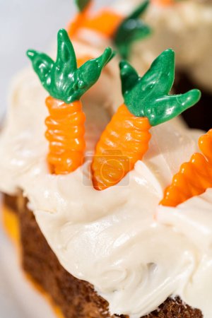Téléchargez les photos : Décorer gâteau bundt aux carottes fraîchement cuit avec glaçage au fromage à la crème avec garnitures gâteau aux carottes au chocolat. - en image libre de droit