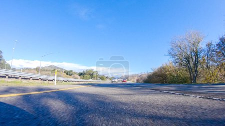 Photo for On a crisp winter day, a car cruises along the iconic Highway 1 near San Luis Obispo, California. The surrounding landscape is brownish and subdued, with rolling hills and patches of coastal - Royalty Free Image