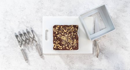 Photo for Flat lay. Removing chocolate hazelnut fudge from a square cheesecake pan lined with parchment. - Royalty Free Image