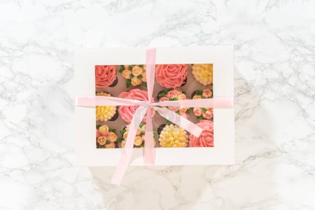 Photo for Encased in a pristine white paper cupcake box, each gourmet cupcake is a work of art, adorned with buttercream frosting flowers beautifully designed to resemble vibrant roses and tulips. - Royalty Free Image