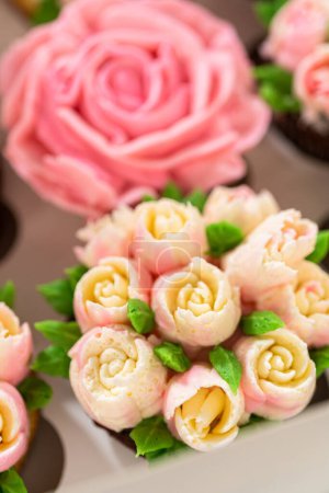 Foto de Encerrado en una caja de cupcakes de papel blanco prístino, cada cupcake gourmet es una obra de arte, adornada con flores de glaseado de crema de mantequilla bellamente diseñadas para parecerse a rosas vibrantes y tulipanes. - Imagen libre de derechos