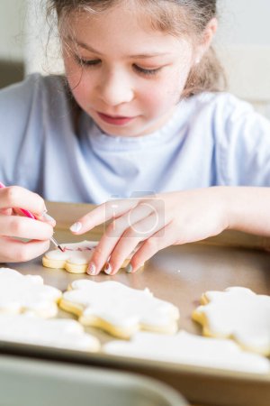 Téléchargez les photos : Une scène chaleureuse d'une petite fille écrivant avec soin Désolé sur les biscuits au sucre avec colorant alimentaire, les biscuits magnifiquement inondés de glaçage royal blanc. - en image libre de droit