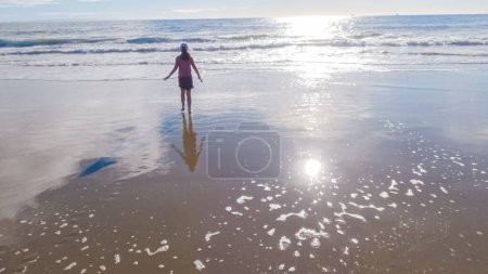Téléchargez les photos : Une petite fille joue joyeusement sur le vaste sable vide de El Capitan State Beach en Californie pendant l'hiver. - en image libre de droit