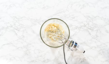 Téléchargez les photos : Pose plate. Mélanger les ingrédients dans un bol à mélanger en verre pour faire le glaçage au fromage à la crème pour les cupcakes sans levure à la cannelle. - en image libre de droit