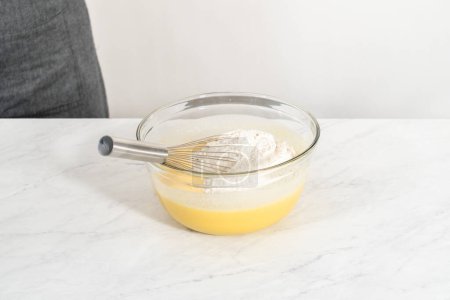 Téléchargez les photos : Mélanger les ingrédients dans un grand bol à mélanger en verre pour faire cuire le gâteau bundt aux myrtilles au citron. - en image libre de droit