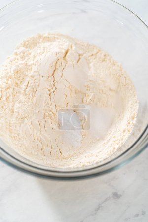 Foto de Mezclar ingredientes secos con un batidor de mano en un tazón de vidrio para hornear pastel de limonada de arándanos. - Imagen libre de derechos
