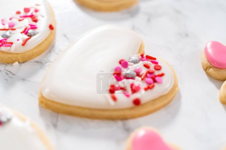 Photo for Decorating heart-shaped sugar cookies with pink and white royal icing for Valentines Day. - Royalty Free Image