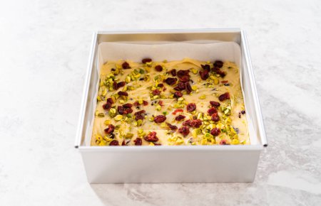 Photo for Filling square cheesecake pan lined with parchment paper with fudge mixture to prepare cranberry pistachio fudge. - Royalty Free Image
