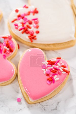 Herzförmige Zuckerkekse zum Valentinstag mit rosa und weißem Zuckerguss verzieren.