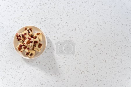 Téléchargez les photos : Pose plate. Pièces de caramel au chocolat blanc à la canneberge et aux noix de pécan sur une plaque en céramique blanche. - en image libre de droit