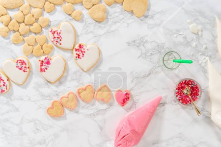Flat lay. Decorating heart-shaped sugar cookies with pink and white royal icing for Valentines Day.