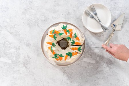 Photo for Flat lay. Slicing freshly baked carrot bundt cake with cream cheese frosting and decorated chocolate carrot cake toppers. - Royalty Free Image