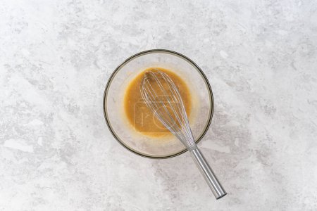 Photo for Flat lay. Mixing wet and dry ingredients with a hand whisk in a glass mixing bowl to bake a carrot bundt cake with cream cheese frosting. - Royalty Free Image