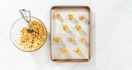 Photo for Flat lay. Scooping cookie batter with dough scoop into a baking sheet lined with parchment paper to bake white chocolate macadamia nut. - Royalty Free Image