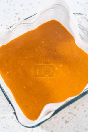 Téléchargez les photos : Verser le mélange de caramel dans le moule en verre carré doublé de papier parchemin pour préparer le caramel à la citrouille. - en image libre de droit