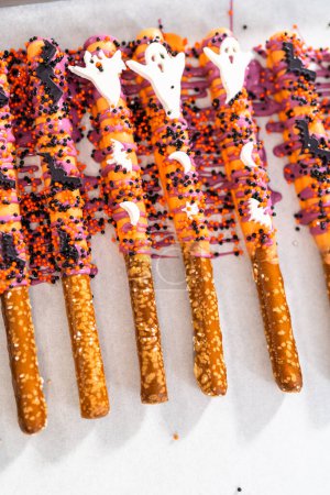 Téléchargez les photos : Tremper les tiges de bretzel dans du chocolat fondu pour faire des tiges de bretzel recouvertes de chocolat Halloween. - en image libre de droit