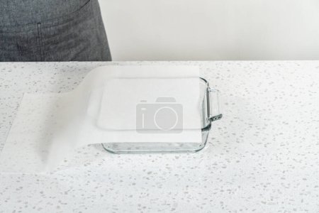 Foto de Revestimiento de vidrio bandeja para hornear con hoja de papel de pergamino para preparar dulce llano. - Imagen libre de derechos