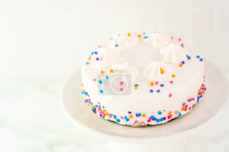 Téléchargez les photos : Petit gâteau d'anniversaire blanc avec des aspersions de funfettis sur une assiette de gâteau blanc. - en image libre de droit