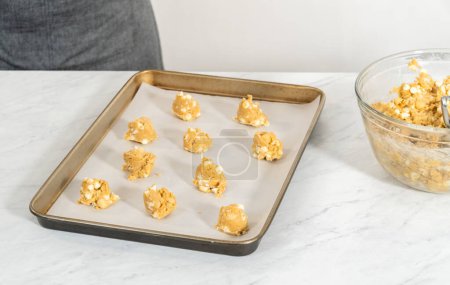 Téléchargez les photos : Cuire la pâte à biscuits avec la pelle à pâte dans une plaque à pâtisserie doublée de papier parchemin pour cuire les noix de macadamia au chocolat blanc. - en image libre de droit