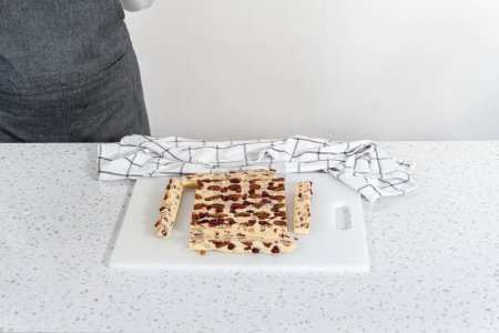 Téléchargez les photos : Découpe de caramel au chocolat blanc aux canneberges en petits morceaux sur une planche à découper blanche. - en image libre de droit