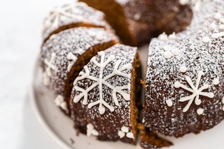 Photo for Sliced gingerbread bundt cake with caramel filling, buttercream frosting, and powdered sugar dusting on the cake plate. - Royalty Free Image