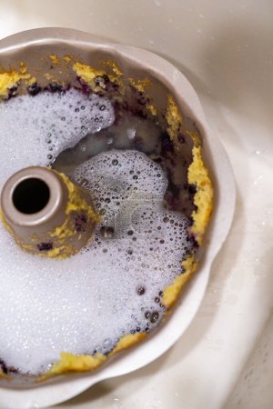 Foto de Remojar la bandeja de pastel de aluminio sucio con agua jabonosa en un fregadero de cocina. - Imagen libre de derechos