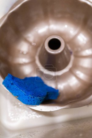 Téléchargez les photos : Frotter la casserole à gâteau en aluminium sale avec une éponge bleue dans un évier de cuisine. - en image libre de droit