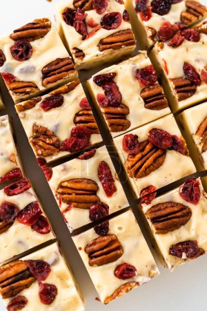Photo for Cutting white chocolate cranberry pecan fudge into small pieces on a white cutting board. - Royalty Free Image