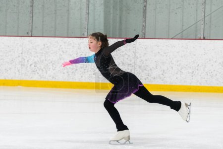 Téléchargez les photos : Jeune fille perfectionnant sa routine de patinage artistique tout en portant sa robe de compétition à une patinoire intérieure. - en image libre de droit