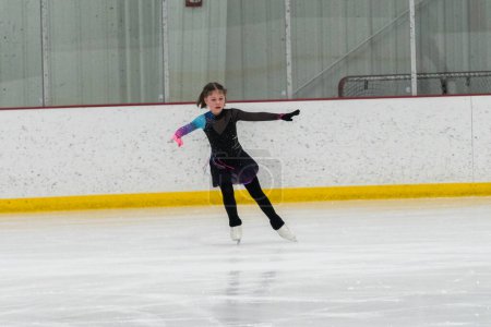 Photo for Young girl perfecting her figure skating routine while wearing her competition dress at an indoor ice rink. - Royalty Free Image
