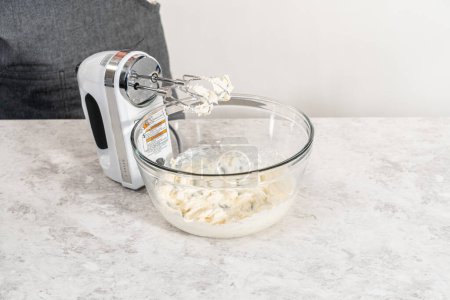 Téléchargez les photos : Mélanger les ingrédients avec un mélangeur à main dans un grand bol à mélanger pour faire du glaçage au fromage à la crème pour gâteau bundt aux carottes. - en image libre de droit