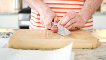 Photo for In the contemporary ambiance of a modern kitchen, a young man engages in dinner preparations. His current activity entails meticulously slicing small rainbow potatoes in half on a wooden cutting board - Royalty Free Image