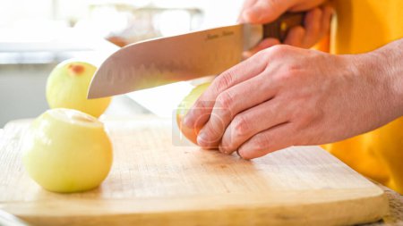 Photo for In the welcoming setting of a modern kitchen, a young man continues his dinner preparation process. Hes currently involved in slicing yellow onions into rings, prepping them for grilling on an - Royalty Free Image