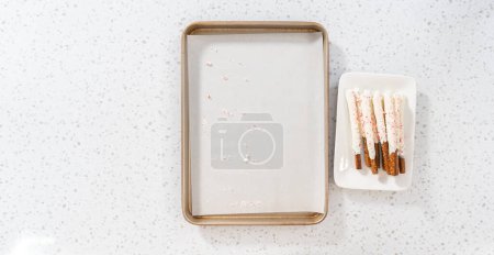 Photo for Flat lay. Transferring homemade candy cane chocolate-covered pretzel rods to a white serving plate. - Royalty Free Image