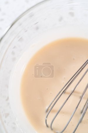 Photo for Mixing ingredients with a hand whisk in a glass mixing bowl to make the vanilla glaze. - Royalty Free Image