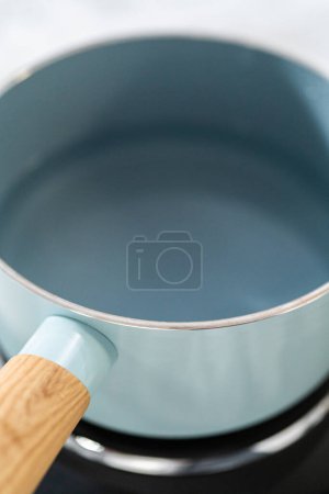 Foto de Derretir chispas de chocolate blanco y otros ingredientes en un recipiente de mezcla de vidrio sobre agua hirviendo para preparar caramelo fudge caña. - Imagen libre de derechos
