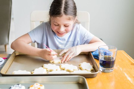 Photo for A heartwarming scene of a little girl carefully writing Sorry on sugar cookies with food coloring, the cookies beautifully flooded with white royal icing. - Royalty Free Image