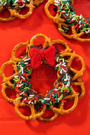Foto de Chocolate pretzel Christmas wreath decorated with sprinkles and red chocolate bow on a red background. - Imagen libre de derechos