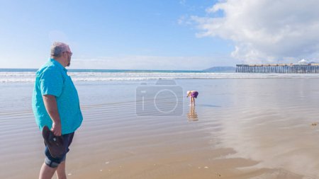 Photo for Father and daughter enjoy a leisurely winter walk along the picturesque Pismo Beach, sharing quality time together amid the serene backdrop of gently crashing waves. - Royalty Free Image