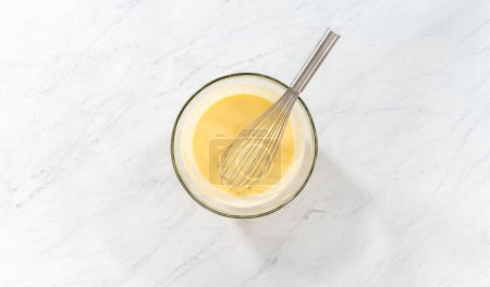 Téléchargez les photos : Pose plate. Mélanger les ingrédients humides dans un grand bol à mélanger en verre pour faire cuire le gâteau bundt aux myrtilles au citron. - en image libre de droit