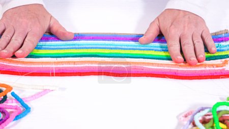 Photo for Hands touch a neatly organized rainbow of colorful, coiled clay bead strands against a contrasting white surface. - Royalty Free Image