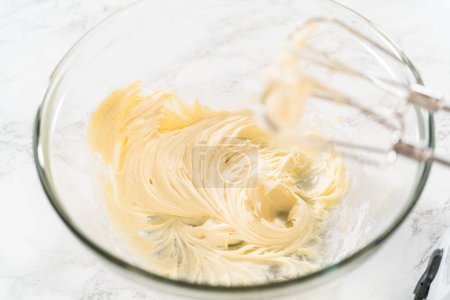 Foto de Mezclar los ingredientes en un tazón de vidrio para hacer el glaseado de queso crema para cupcakes de canela sin levadura. - Imagen libre de derechos