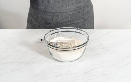 Foto de Acostado. Mezclar ingredientes secos con un batidor de mano en un tazón de vidrio para hornear pastel de limonada de arándanos. - Imagen libre de derechos