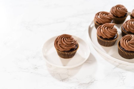 Photo for Freshly baked cupcakes have been masterfully infused with rich caramel and adorned with velvety chocolate frosting, all elegantly presented on a pristine white serving plate. - Royalty Free Image