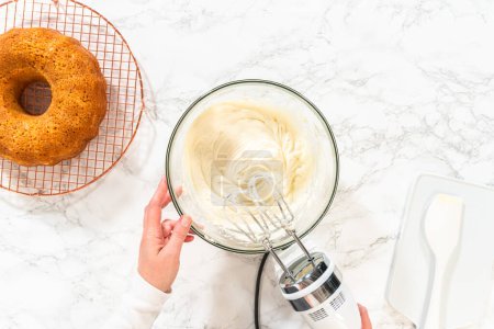 Téléchargez les photos : Dans un grand bol à mélanger, les ingrédients sont savamment mélangés pour créer une crème au beurre au fromage à la crème délectable pour le gâteau Bundt aux carottes. - en image libre de droit