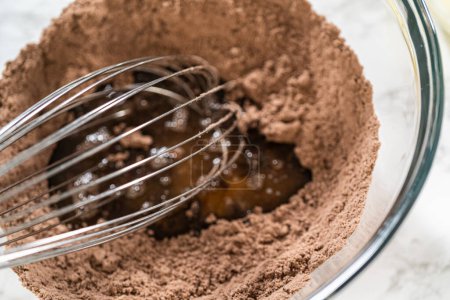 Foto de En el proceso de crear deliciosos cupcakes de chocolate, el primer paso consiste en mezclar meticulosamente los ingredientes en un tazón de vidrio para hacer la masa perfecta.. - Imagen libre de derechos