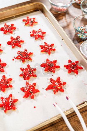 Photo for Vivid red star-shaped cookies, generously iced and speckled with green and white holiday sprinkles, freshly prepared and laid out to dry. - Royalty Free Image